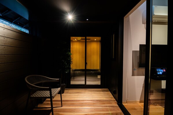 A modern interior with a wooden bench, a potted plant, and a glass door leading to a room with a sliding door.