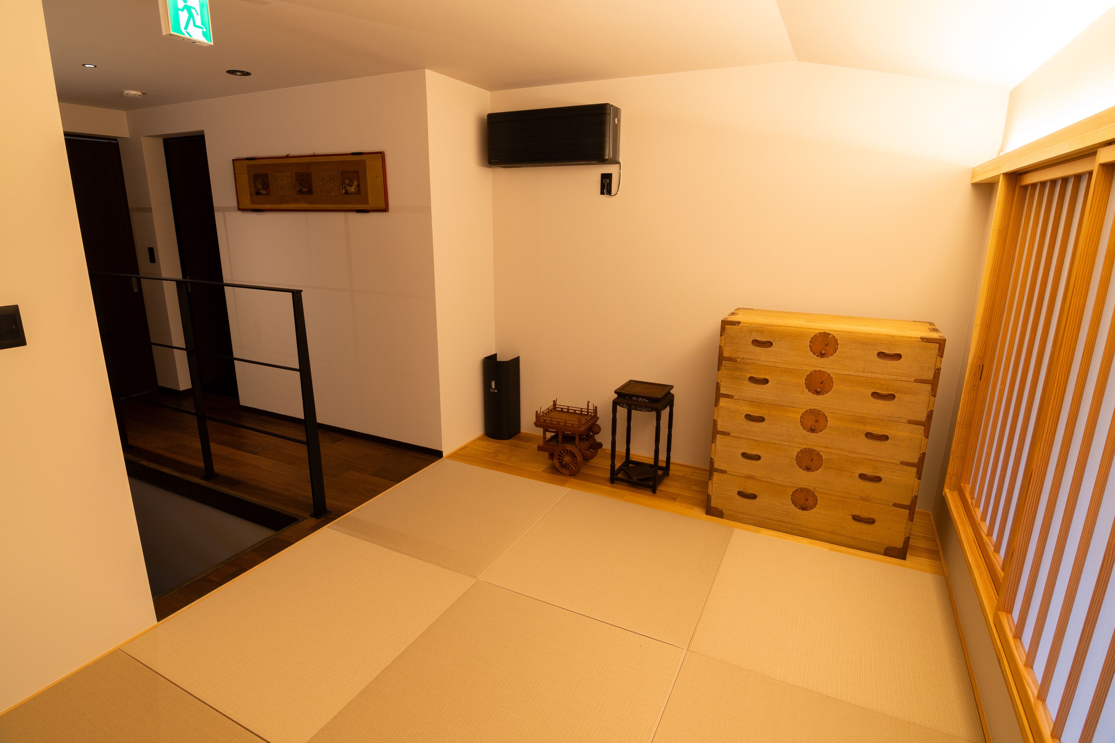 A room with tatami mats, a wooden chest, a small table, and a wall-mounted air conditioner.