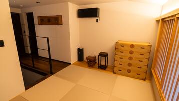 A room with tatami mats, a wooden chest, a small table, and a wall-mounted air conditioner.