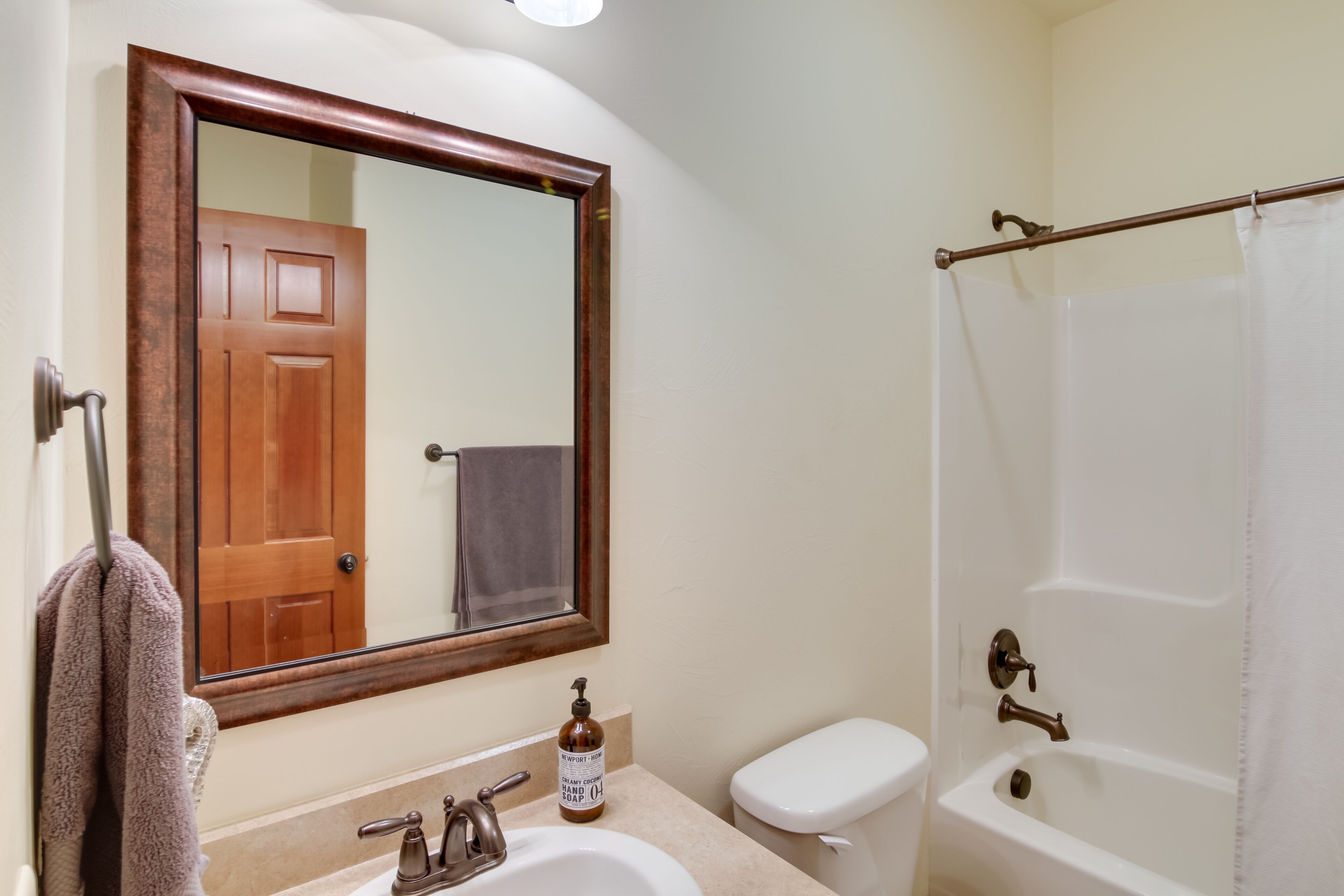 A bathroom with a wooden-framed mirror, a sink with a soap dispenser, a toilet, and a bathtub with a shower curtain.