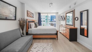 A modern bedroom with a bed, a grey sofa, a dresser, and a large window offering a city view. - Great Apartment in the heart of Brickell (Miami)