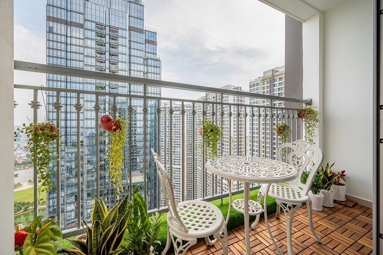 A balcony with a white metal railing, two white chairs, a small round table, and potted plants.