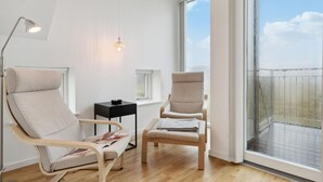 A modern living room with two beige armchairs, a small black side table, a floor lamp, and a large window offering a view of the sky and a fence. - Beautiful home in Skagen with WiFi (Skagen)