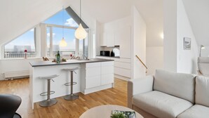 A modern kitchen with a large window, white cabinetry, and a dining area with a sofa and bar stools. - Beautiful home in Skagen with WiFi (Skagen)