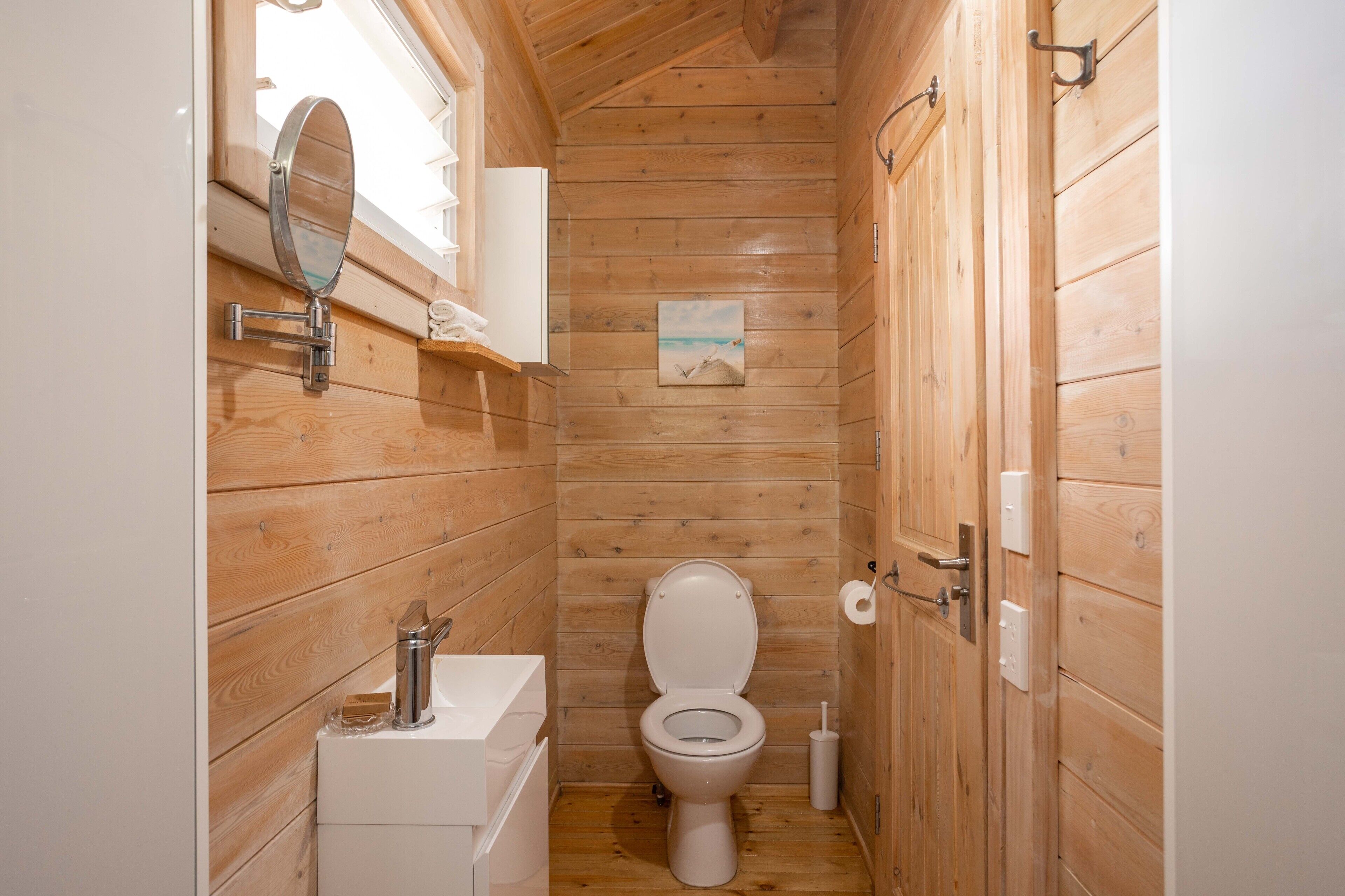 A small wooden cabin bathroom with a toilet, sink, and a mirror.