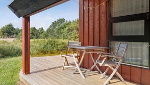 Una terraza de madera con una mesa, dos sillas, una ventana y vistas a un área boscosa.