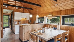 Interior de una cabaña de madera con cocina, comedor y ventanas amplias.