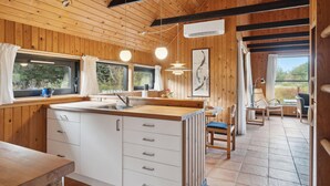 Interior de una cabaña con detalles de madera, una zona de cocina con lavamanos y armarios, y un comedor con sillas y mesa.