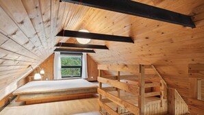 Un dormitorio en un ático con techo inclinado, un ventanal grande y un banco de madera empotrado.