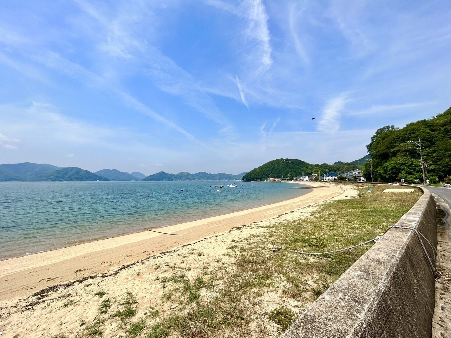A beach with a concrete barrier, calm water, and distant mountains.