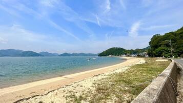 A beach with a concrete barrier, calm water, and distant mountains.