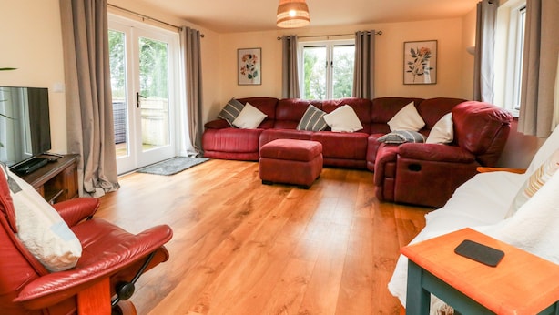 A spacious living room with a red leather sofa set, a wooden floor, and a television on a wooden stand.