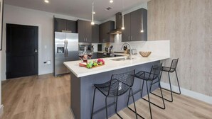 A modern kitchen with a central island, bar stools, stainless steel appliances, and pendant lighting. - Tune - Odyssey - Pool & Gym - Mins to Broadway! (Nashville)