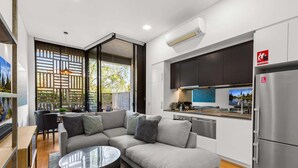 Una cocina moderna con horno integrado, un refrigerador de acero inoxidable y un comedor con sofá y una mesa de centro.