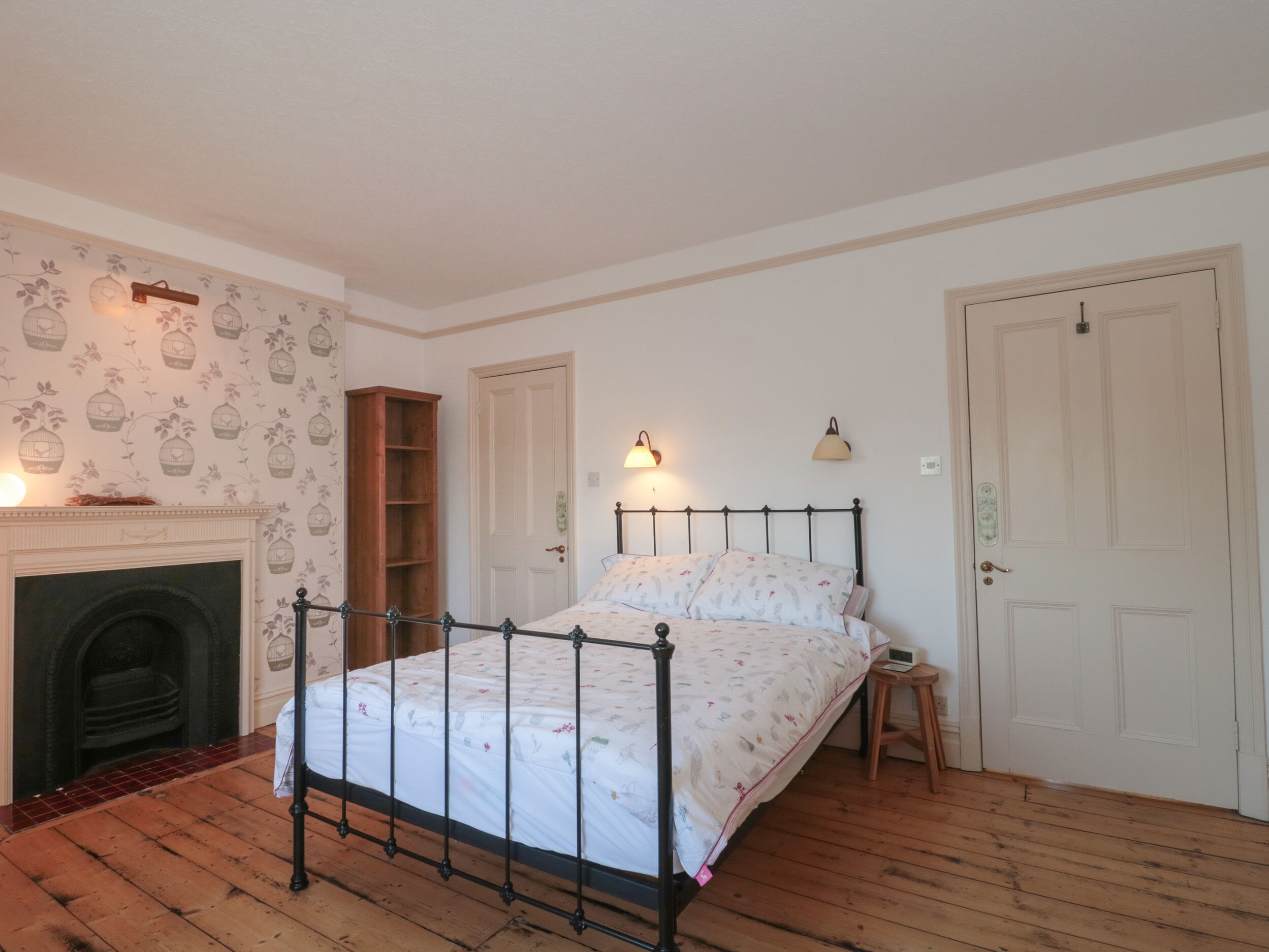 A bedroom with a four-poster bed, a fireplace, a wooden bookshelf, and two doors.