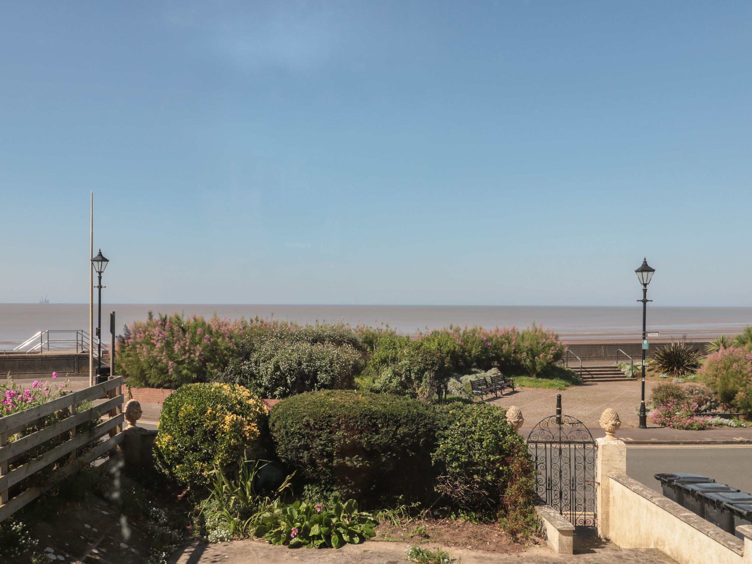 A coastal garden with a paved walkway, benches, and a view of the sea.