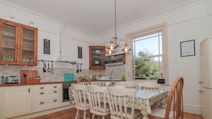 Una cocina con armarios de madera, una mesa de comedor con cuatro sillas, una lámpara colgante y una ventana con vistas a árboles.
