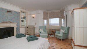 Un dormitorio con una cama, dos sillones, un aparador, una chimenea y vista al mar.