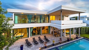 Une maison moderne à deux étages, dotée d’une piscine, d’un espace salon extérieur et de grandes fenêtres.