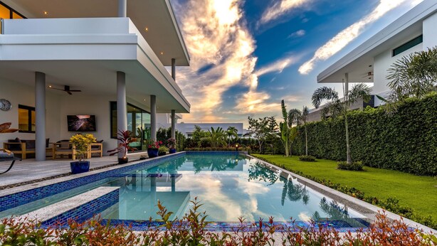 Un espace piscine moderne offrant une vue dégagée sur le ciel, une pelouse bien entretenue et un coin salon avec des meubles d’extérieur.