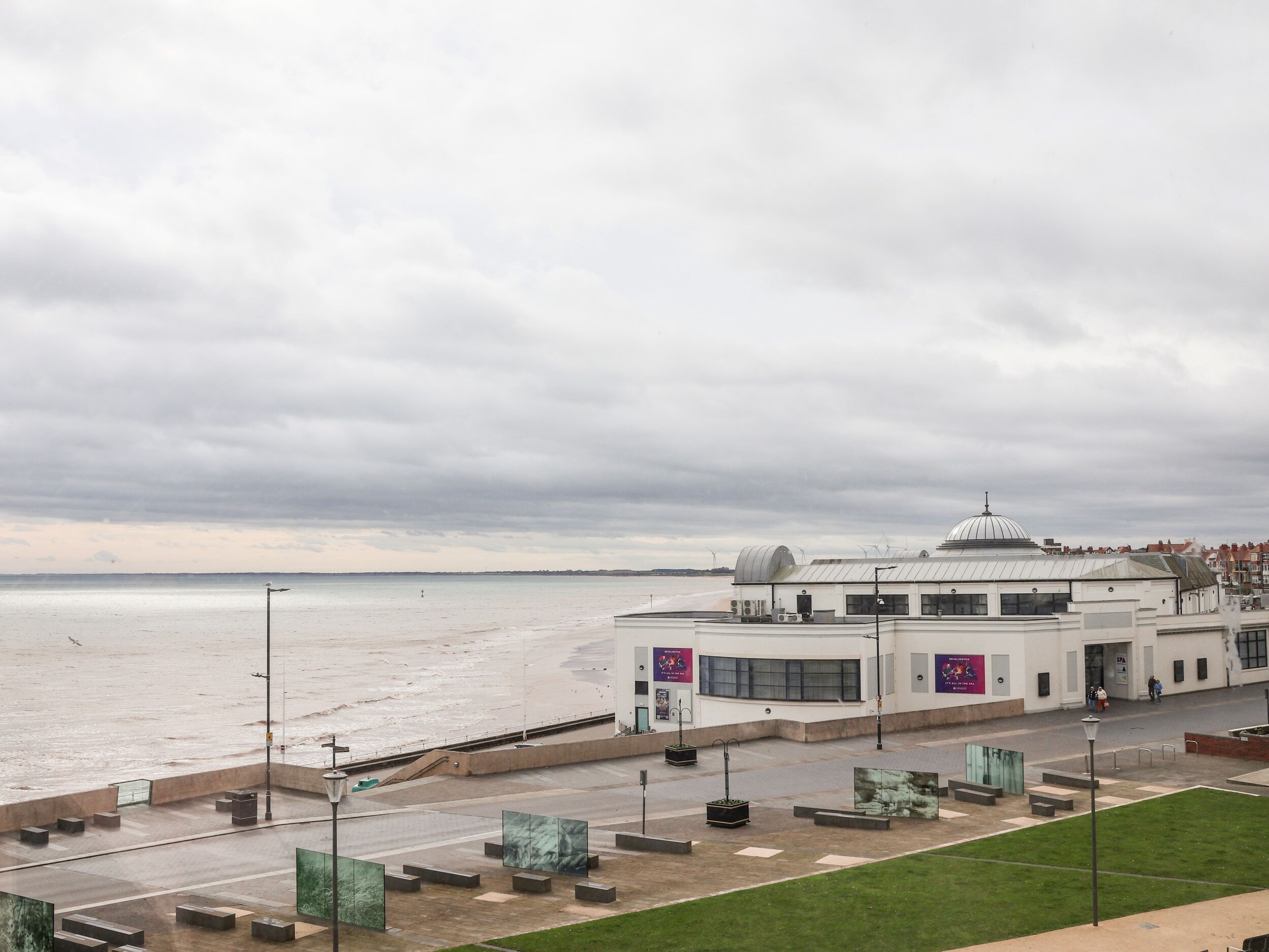 A coastal building with a dome, a paved walkway, and a grassy area.