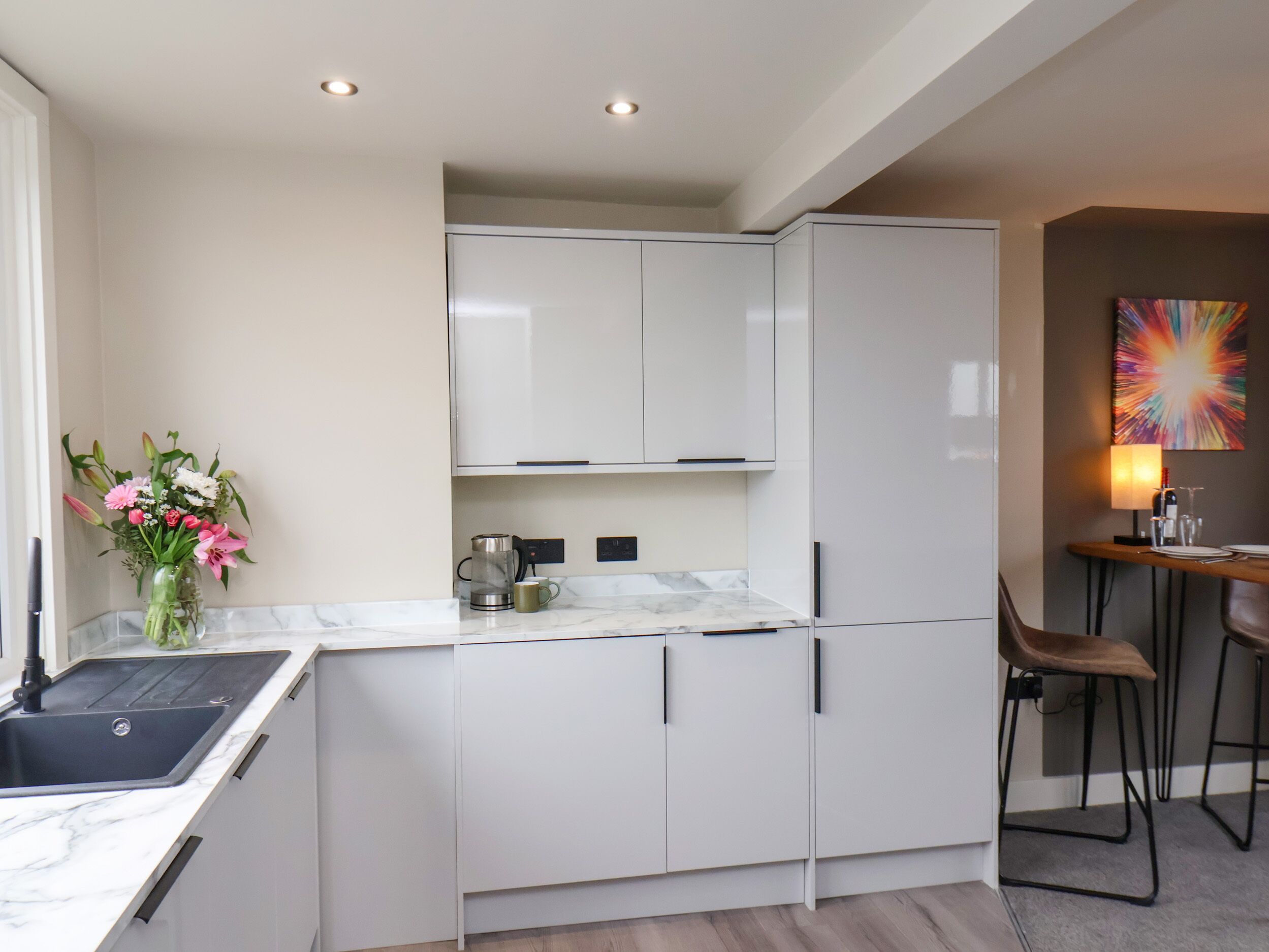 A modern kitchen with white cabinets, a marble countertop, a coffee maker, and a vase of flowers.