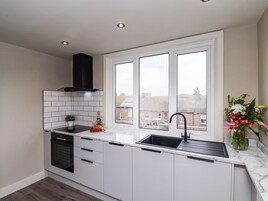 A modern kitchen with white cabinets, a black range hood, a built-in oven, a sink, and a window with a view of buildings.