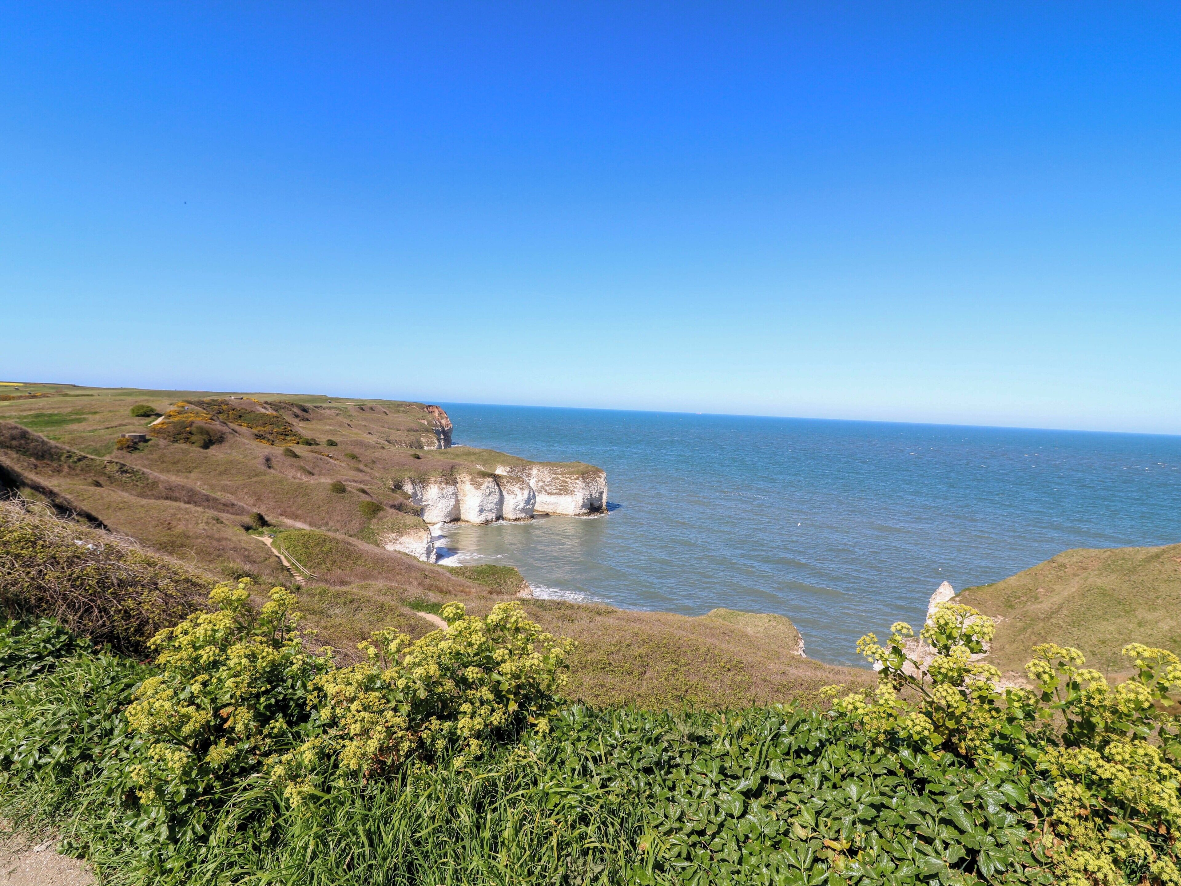 A coastal landscape with cliffs, greenery, and a clear sky.