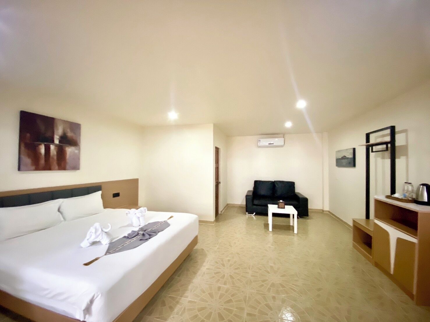 A hotel room with a bed, a black sofa, a small table, and a TV stand.