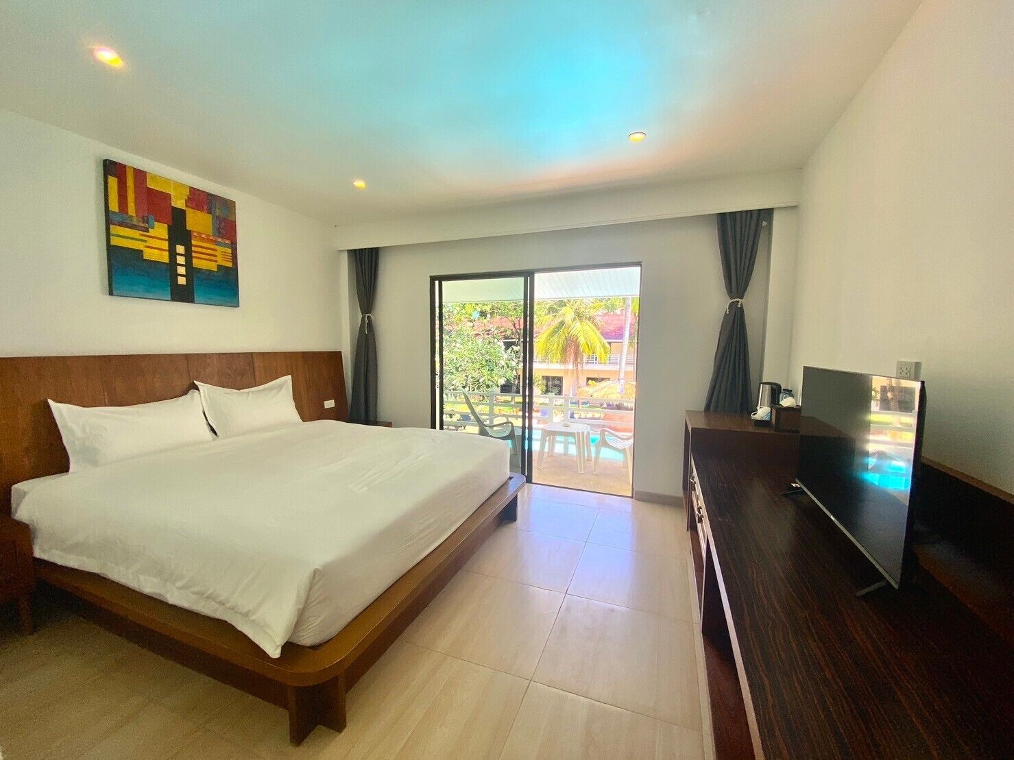 A hotel room with a large bed, a flat-screen TV, and a balcony with a pool view.