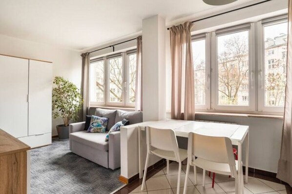 Relax in this serene space with a sofa, dining table, and potted plant, offering a view of the outside.