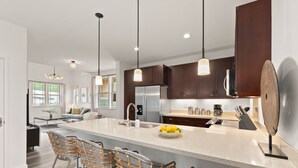 A modern kitchen with a large island, dark wooden cabinets, stainless steel appliances, and a bar area with wicker chairs. - Amazing Ocean Views, Game Room & Modern Design | Aloha Breeze 932 by AvantStay (Waianae)