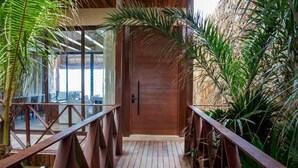 Un sentier en bois mène à une porte, entourée d’une végétation luxuriante et bordée d’une rambarde en bois.