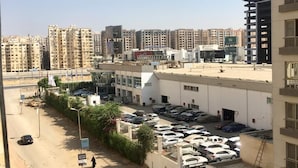 Un estacionamiento con varios autos, un edificio de techo plano y varios rascacielos al fondo.