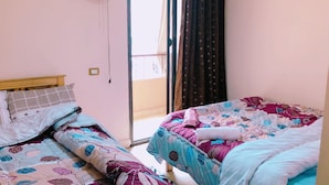 Un dormitorio con dos camas, cada una con ropa de cama estampada. Hay una ventana con cortinas y una puerta que da al exterior.