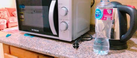 Une cuisine équipée d’un four à micro-ondes, d’une bouilloire et d’une bouteille d’eau posée sur le plan de travail.