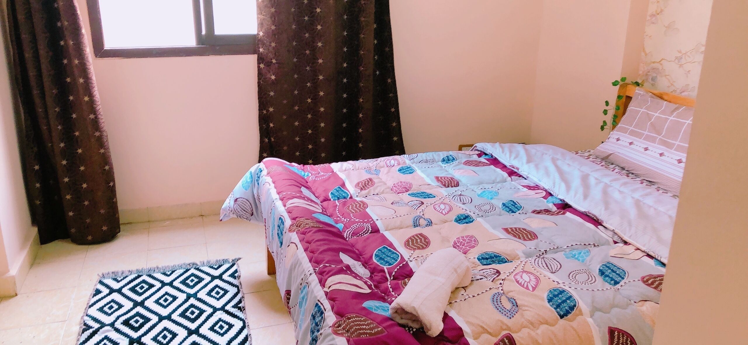 Une chambre à coucher avec un lit, une fenêtre, des rideaux et un tapis à motifs.