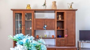 A wooden cabinet with multiple shelves and drawers, a television on a stand, and a floral arrangement on a table. - Vacation home Enrica by Interhome (Marina di Mancaversa)