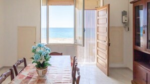 A dining area with a table set for four, a potted plant, and a view of the sea through an open door. - Vacation home Enrica by Interhome (Marina di Mancaversa)