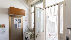 A laundry room with a washing machine, a wooden cabinet, and a door with a window. - Vacation home Enrica by Interhome (Marina di Mancaversa)