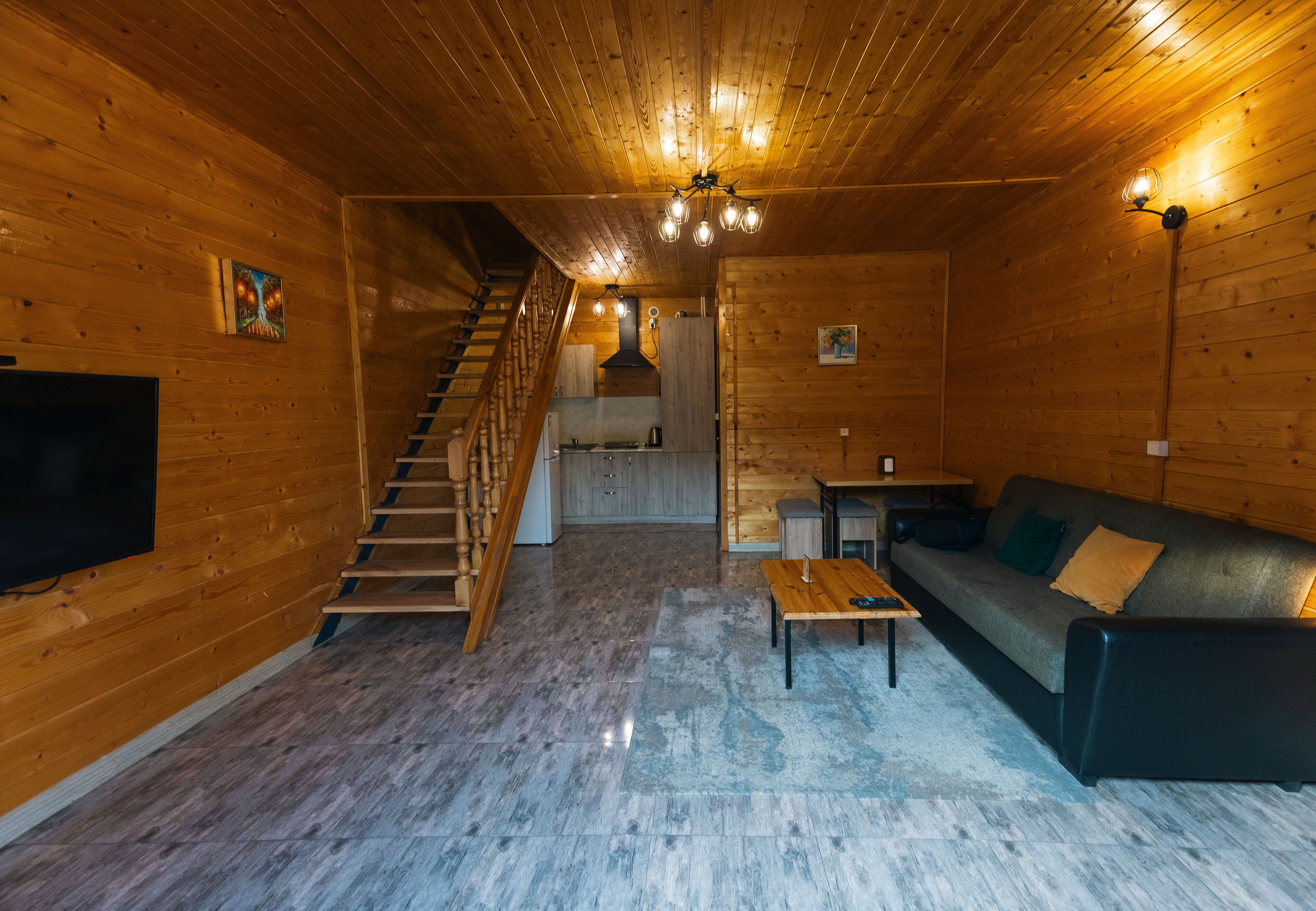 L’intérieur d’une cabane en bois, avec un escalier, un canapé, une table et un téléviseur.