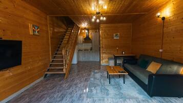 L’intérieur d’une cabane en bois, avec un escalier, un canapé, une table et un téléviseur.
