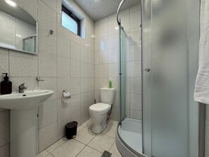 Une salle de bain moderne avec une douche à parois de verre, des toilettes blanches et un lavabo équipé d’un distributeur de savon.