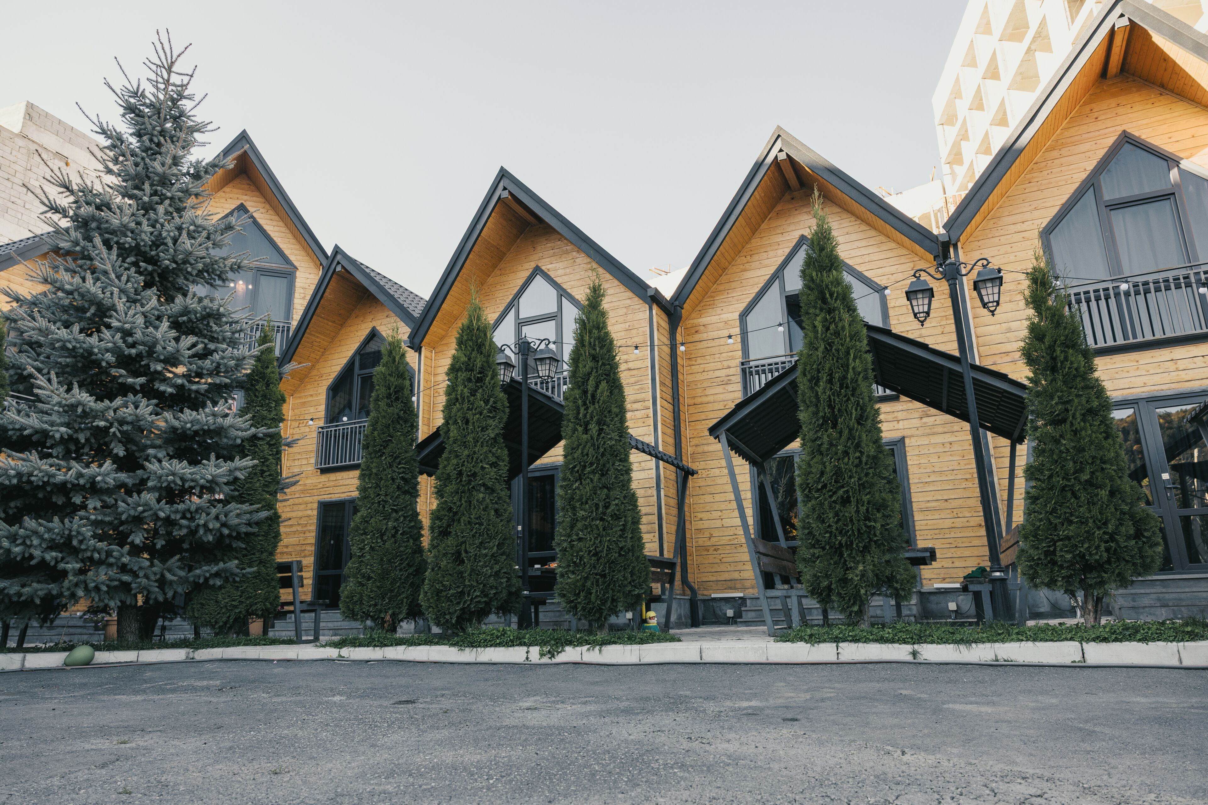 A row of wooden cabins with balconies, a central walkway, and a large tree to the left.