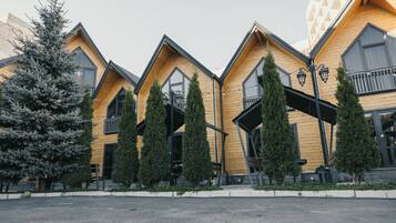 A row of wooden cabins with balconies, a central walkway, and a large tree to the left.