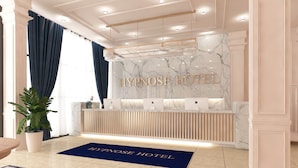 A hotel reception area with a marble wall, a reception desk, and a potted plant. - Hypnose Hotel (Lubumbashi)