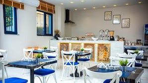 A modern dining area with white and blue chairs, a central island with kitchen appliances, and framed artwork on the walls. - Hypnose Hotel (Lubumbashi)