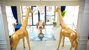 Two golden giraffe statues in a lobby with a chandelier, a patterned rug, and a view of the street outside. - Hypnose Hotel (Lubumbashi)