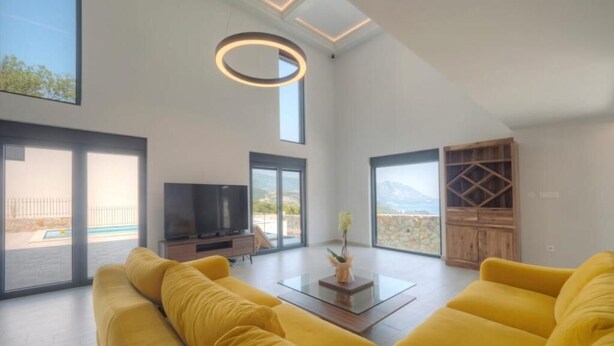 A spacious living room with a large sofa, a coffee table, and a television. There are large windows offering a view of the outdoors. - Seaview Villa with pool Vanja (Podostrog)