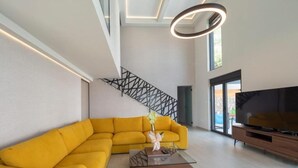 A modern living room with a yellow sectional sofa, a glass coffee table, a TV, and a staircase with a geometric railing. - Seaview Villa with pool Vanja (Podostrog)